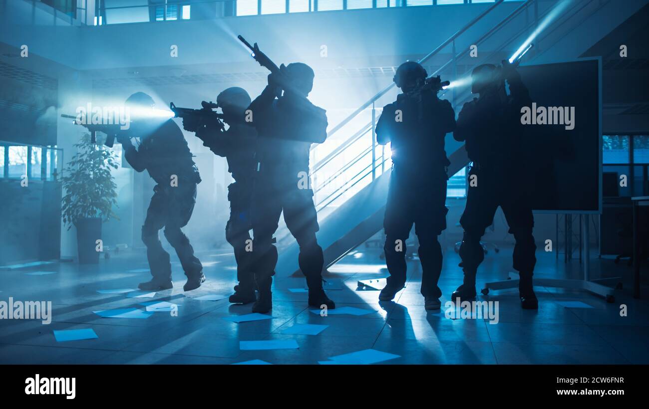 Maskiertes Feuerteam bewaffneter SWAT-Polizeibeamte stürmen ein dunkles beschlagnahmtes Bürogebäude mit Schreibtischen und Computern. Soldaten mit Gewehren und Taschenlampen bewegen sich Stockfoto