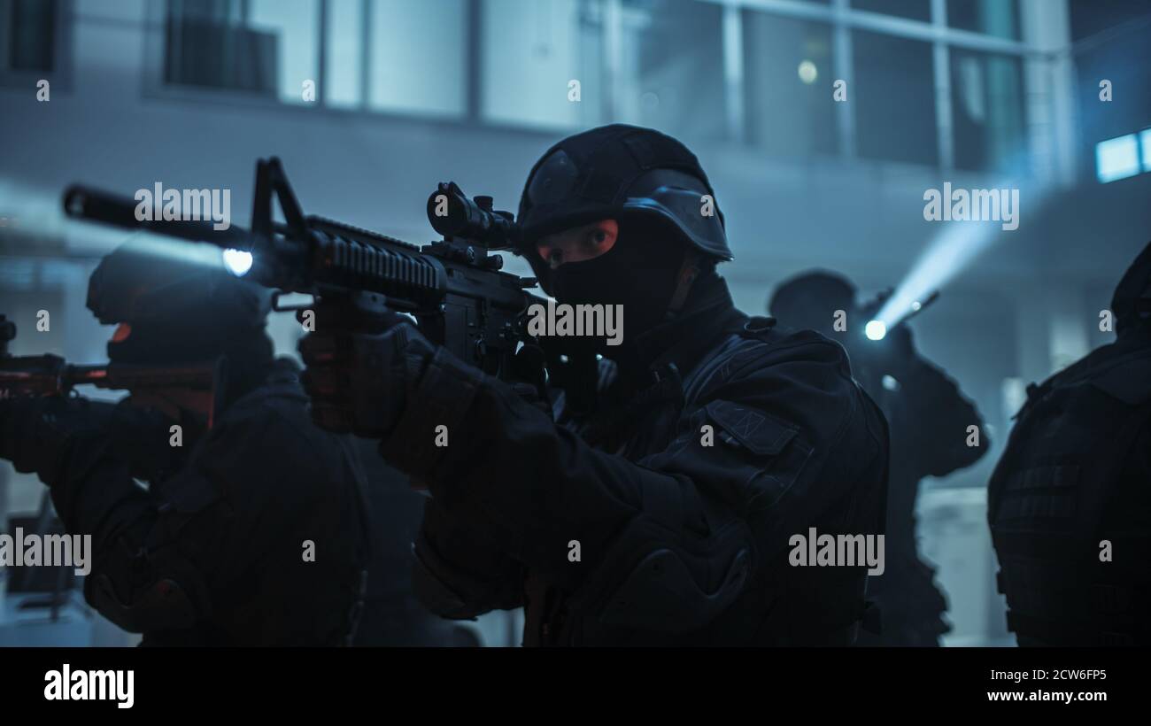 Maskierte Truppe bewaffneter SWAT-Polizisten steht im dunklen beschlagnahmten Bürogebäude mit Schreibtischen und Computern. Soldaten mit Gewehren und Taschenlampen surveil Stockfoto