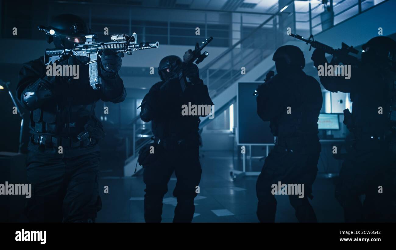 Maskierte Truppe bewaffneter SWAT-Polizisten stürmt ein finsteres beschlagnahmtes Bürogebäude mit Schreibtischen und Computern. Soldaten mit Gewehren und Taschenlampen bewegen sich Stockfoto