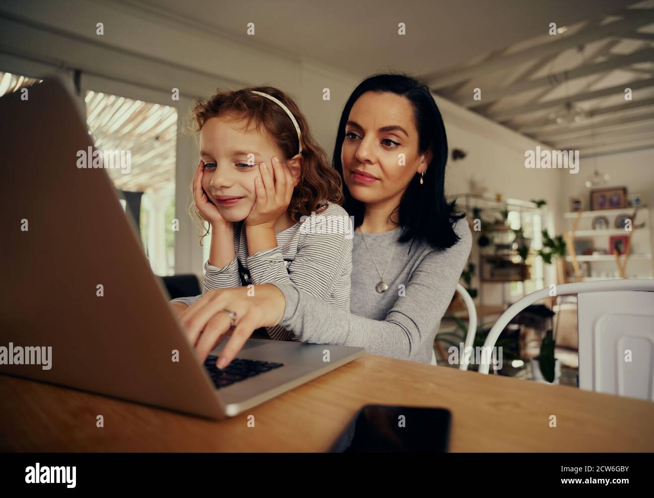 Junge Frau mit einem Laptop-Computer für die Arbeit zu Hause Mit Tochter auf dem Schoß sitzend - Familienbindezeit Stockfoto