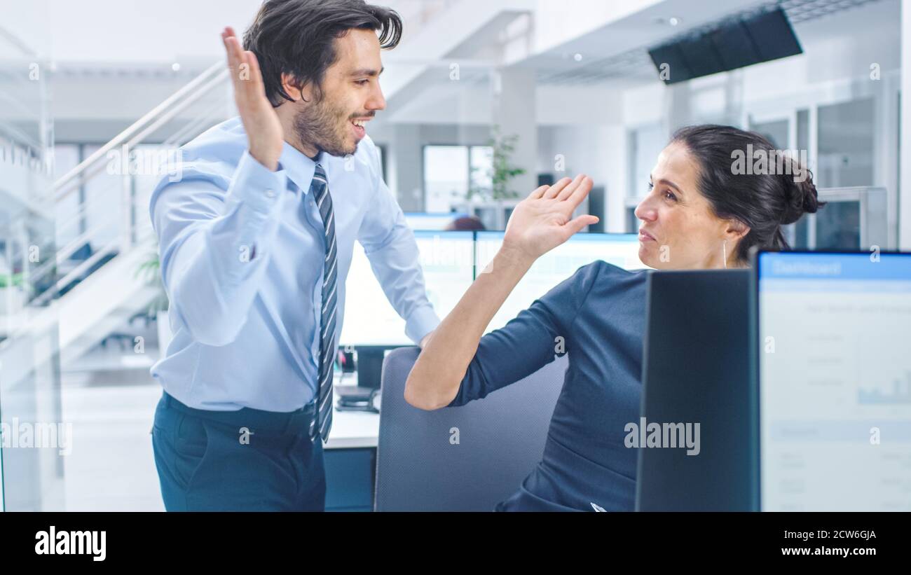 Zwei professionelle Büroangestellte arbeiten am Desktop-Computer, zusammen Finden Sie Lösung für ein Problem und feiern fröhlich Erfolg, indem sie High Five Stockfoto