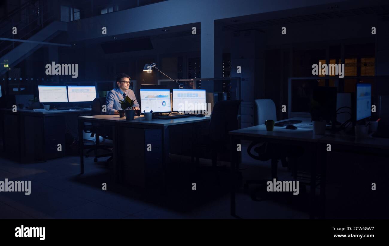 Arbeiten spät in der Nacht im Büro: Geschäftsmann nutzt Desktop-Computer, Analyse, mit Dokumenten, Probleme lösen, wichtige Projekt abschließen Stockfoto