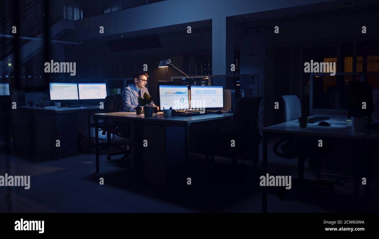 Arbeiten spät in der Nacht im Büro: Geschäftsmann nutzt Desktop-Computer, Analyse, mit Dokumenten, Probleme lösen, wichtige Projekt abschließen Stockfoto