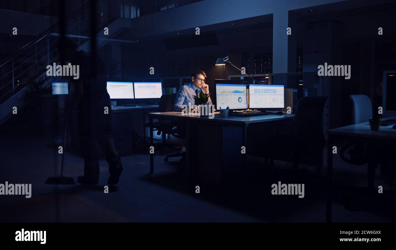 Arbeiten spät in der Nacht im Büro: Geschäftsmann nutzt Desktop-Computer, Analysieren, Verwenden von Dokumenten, Lösen von Problemen, Abschluss wichtiger Projekt Stockfoto