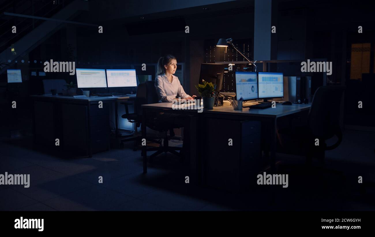 Arbeiten spät in der Nacht im Büro: Geschäftsfrau nutzt Desktop-Computer, analysieren, mit Dokumenten, Probleme lösen, wichtige Projekt abschließen Stockfoto