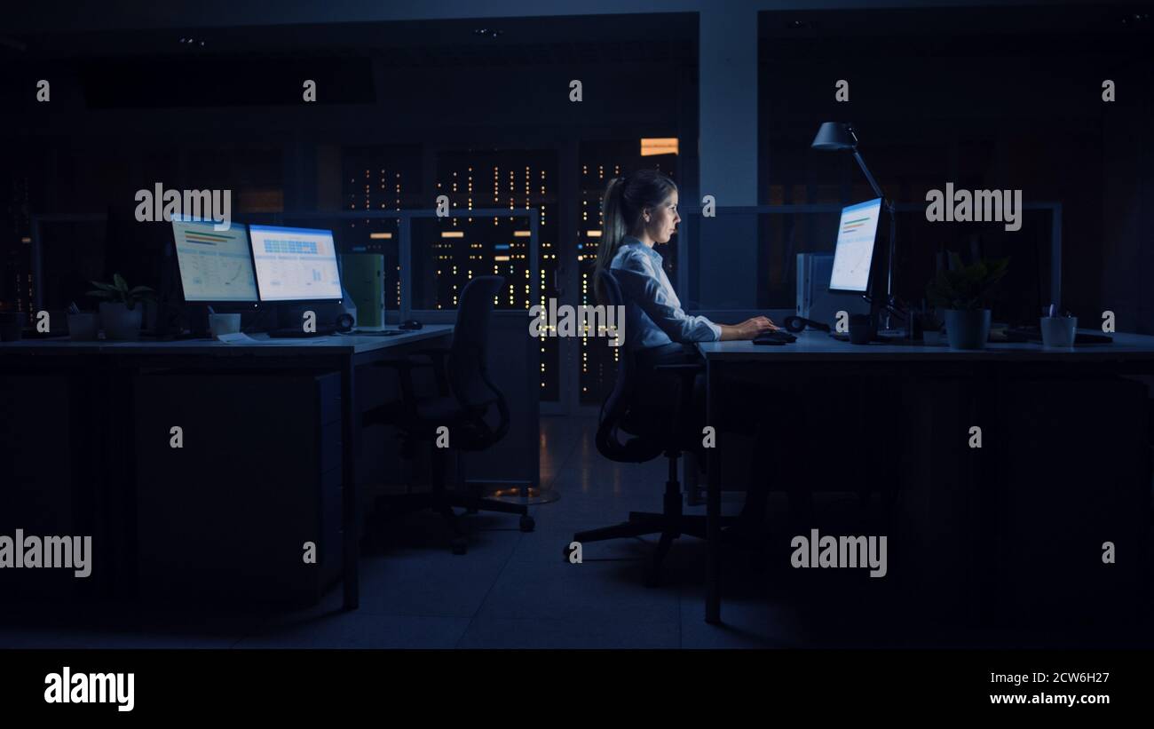 Arbeiten spät in der Nacht im Büro: Geschäftsfrau nutzt Desktop-Computer, analysieren, mit Dokumenten, Probleme lösen, wichtige Projekt abschließen Stockfoto