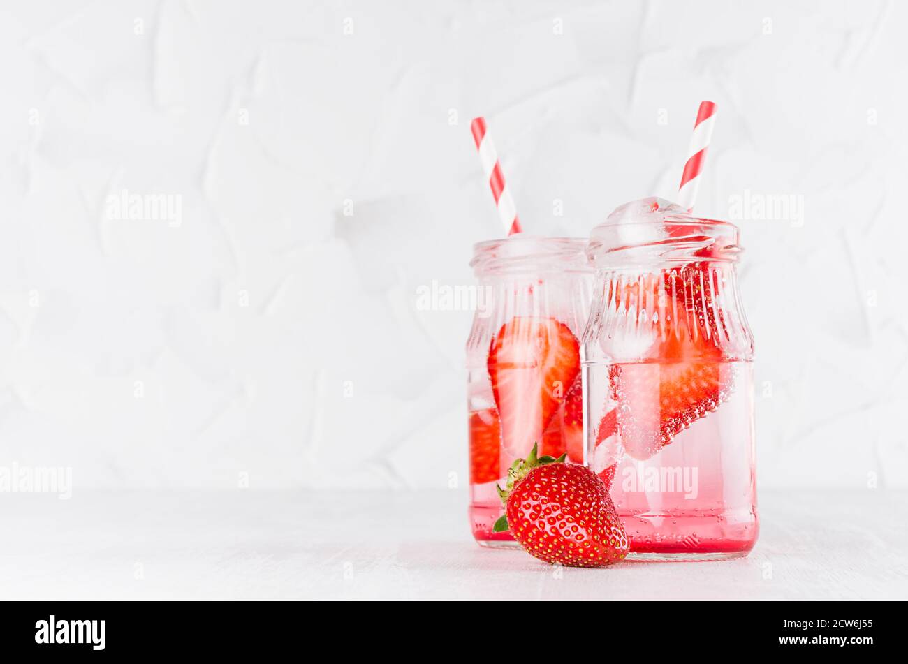 Frische Sommercocktails mit reifen Erdbeeren, Soda, Stroh, Eiswürfeln auf eleganter, hellweißer Holzplatte und Gipswand. Stockfoto