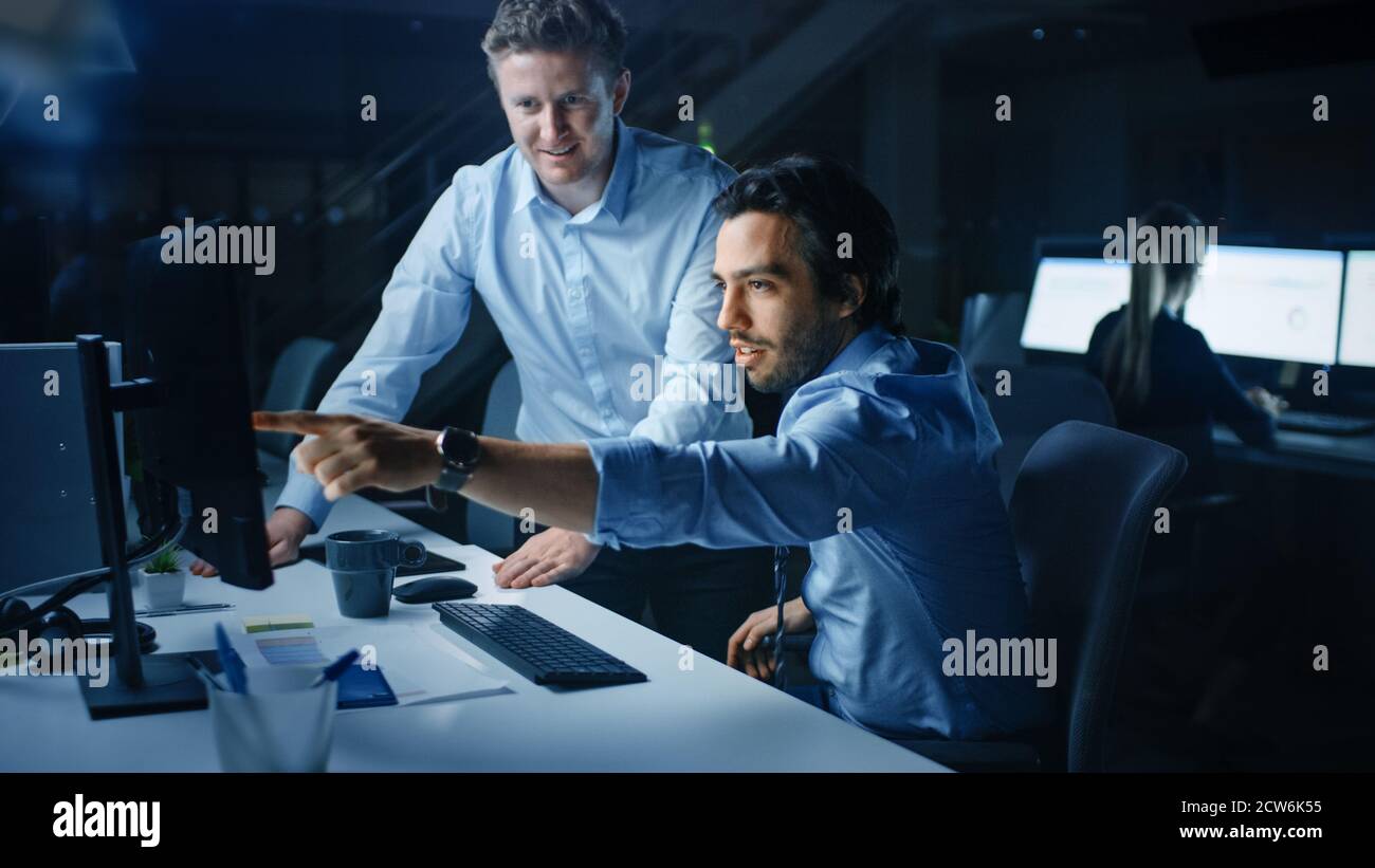 Ehrgeiziger und selbstbewusster Geschäftsmann nutzt Desktop-Computer, sein Projektmanager erklärt spezifische Aufgaben, Account-Handling und strategische Schritte Stockfoto