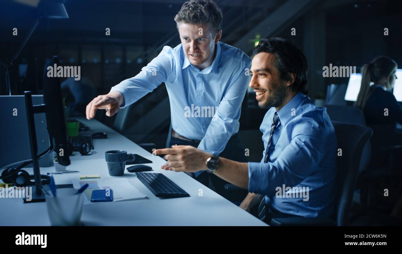 Ehrgeiziger und selbstbewusster Geschäftsmann nutzt Desktop-Computer, sein Projektmanager erklärt spezifische Aufgaben, Account-Handling und strategische Schritte Stockfoto