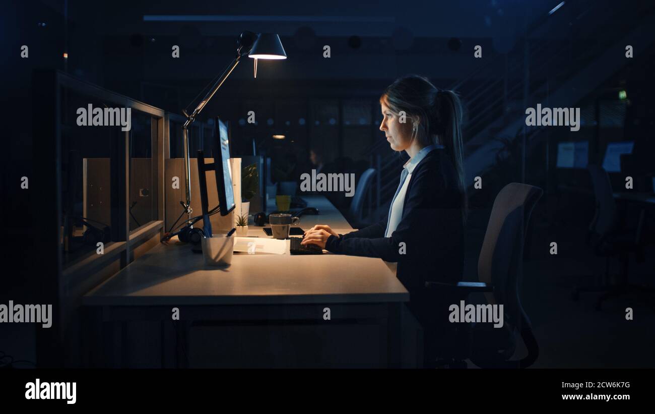 Arbeiten spät in der Nacht im Büro: Geschäftsfrau mit Desktop-Computer, Analysieren, mit Dokumenten, Probleme lösen, Projekt abschließen. Stockfoto