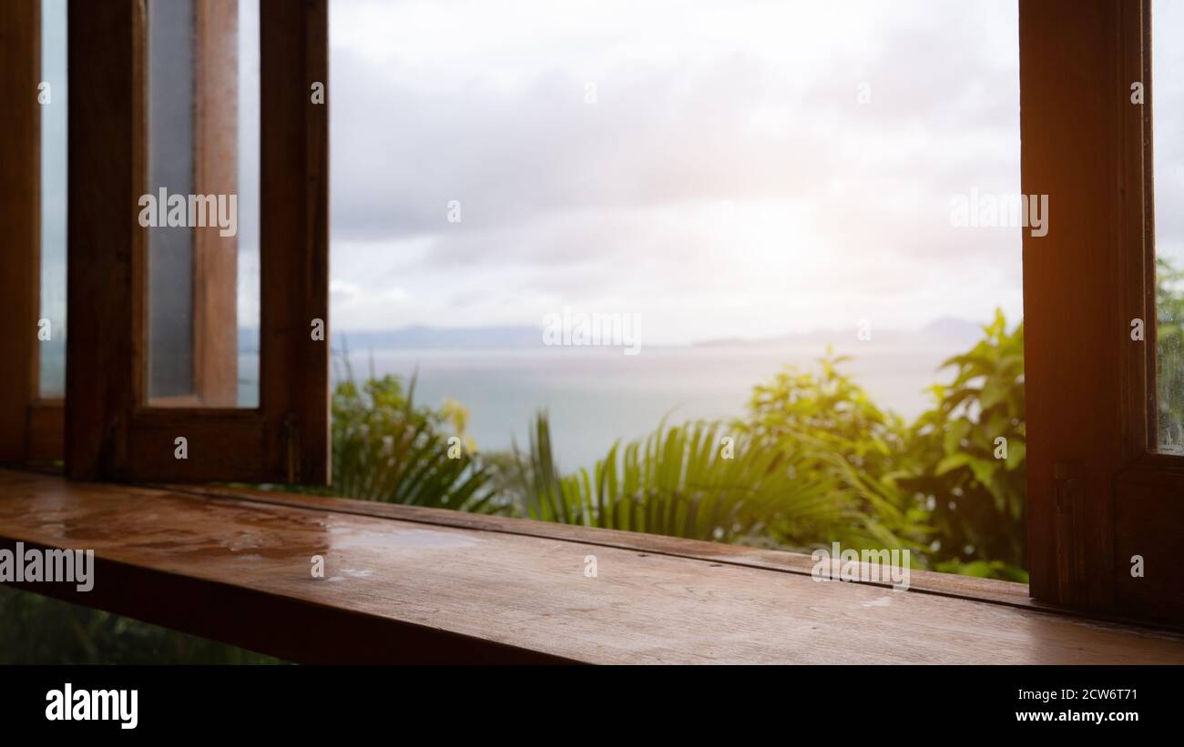 Holztischplatte (Bar) mit Unschärfe auf grünen Palmblättern Oder Baum im tropischen Wald mit Himmel und Meer Hintergrund: Verwendung der Mock-up-Vorlage für die Anzeige Stockfoto