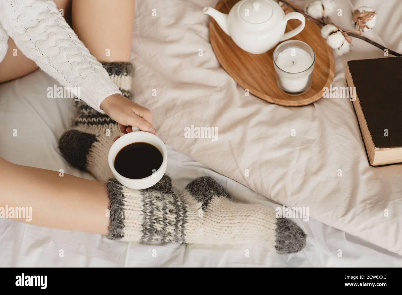 Teilansicht der Frau in gestrickten Socken auf dem Bett mit einer Tasse Kaffee in der Hand. Draufsicht. Stockfoto