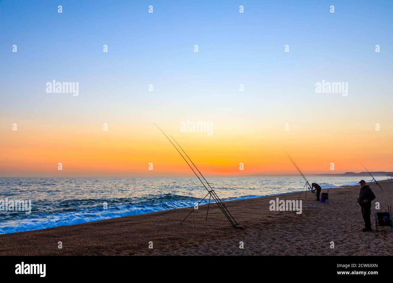 Angelruten und Sonnenuntergang am Strand von West Bexington, einem Dorf im Südwesten von Dorset, England, gelegen hinter Chesil Beach in der Nähe von Bridport, bei Sonnenuntergang Stockfoto