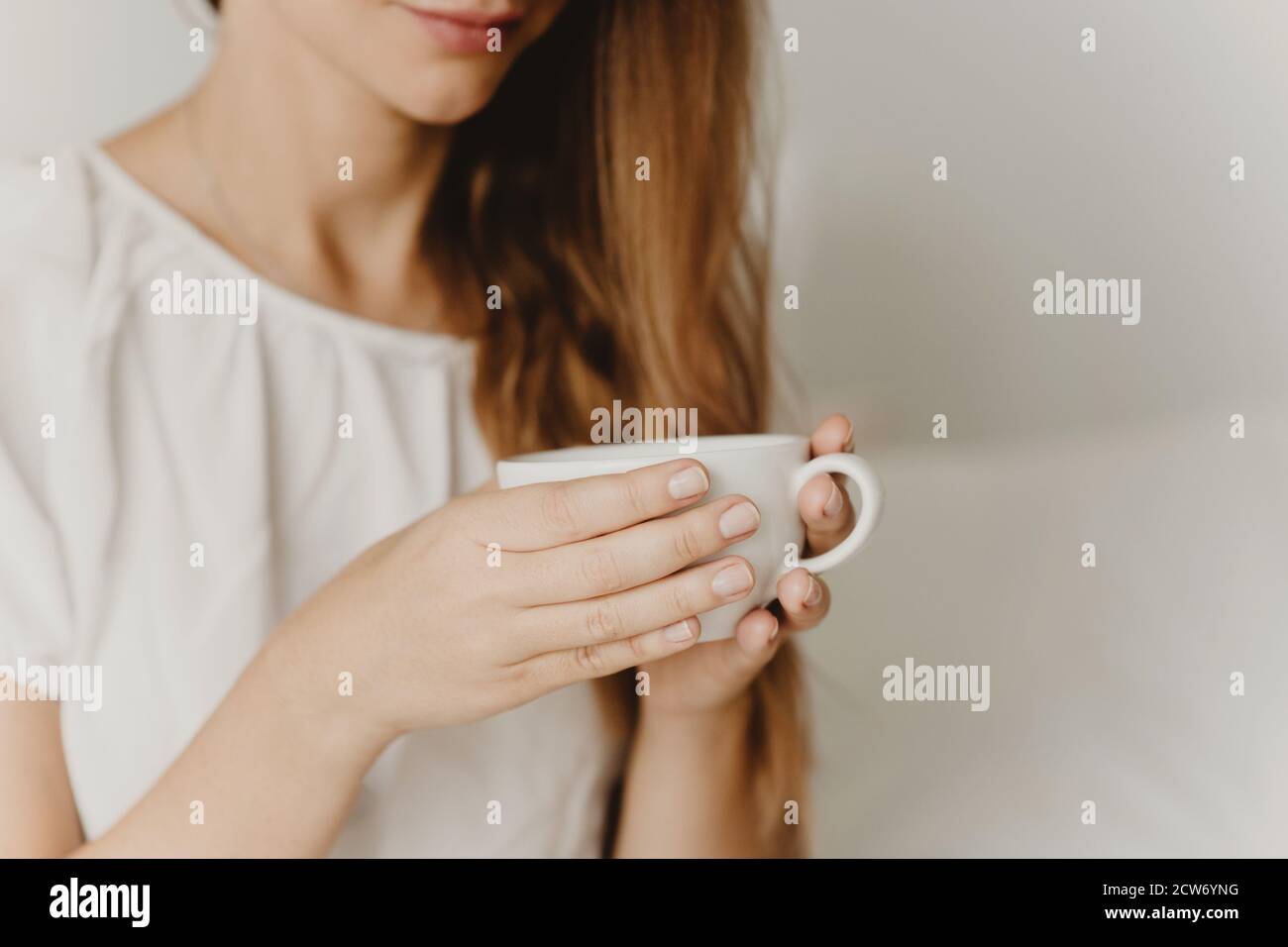 Beschnittene Ansicht der Frau mit langen Haaren hält Tasse Kaffee oder Tee Nahaufnahme. Stockfoto