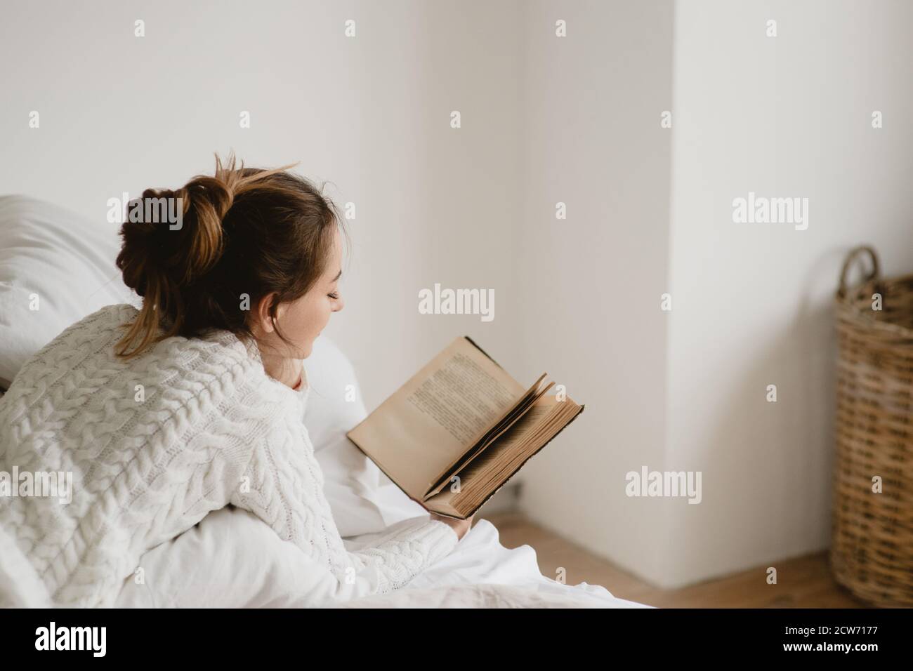Junge Frau in weiß gestrickt Pullover Lesen Buch im Bett zu Hause. Stockfoto