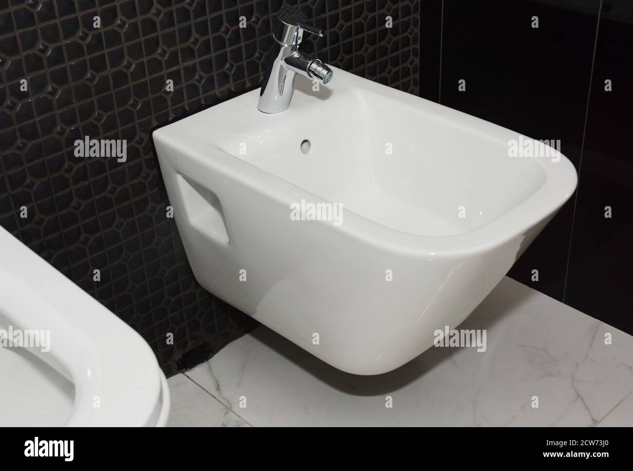 Eine Nahaufnahme auf Keramik einteilige Wand hing Frauen sauber, feminine Hygiene Bidet WC auf einem schwarzen Mosaik gefliesten Wand installiert. Stockfoto