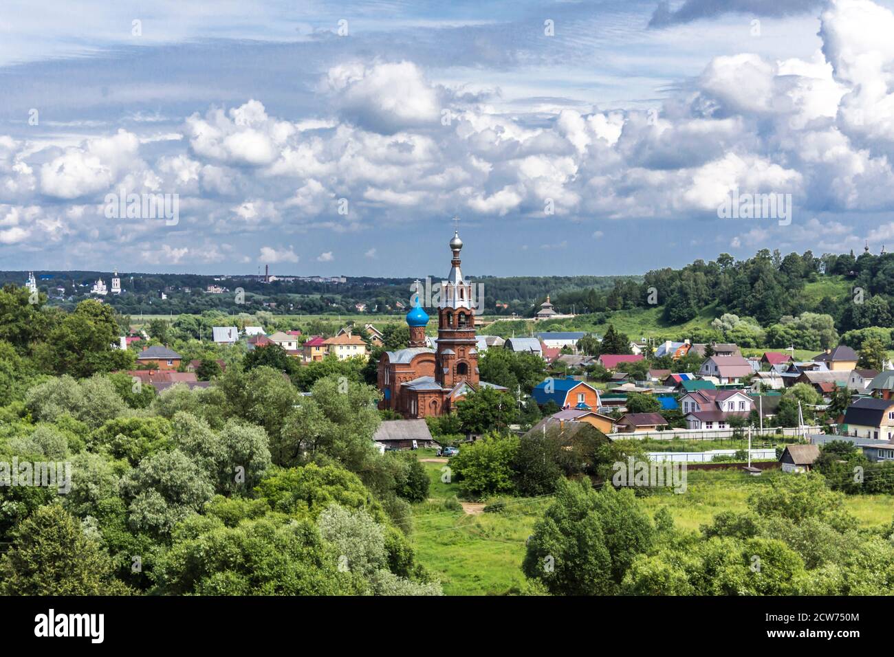 Mittsommer. Backsteinkirche zwischen Hütten und grünen Bäumen. Blick vom Hügel. Provinzstadt Borowsk in Russland. Stockfoto