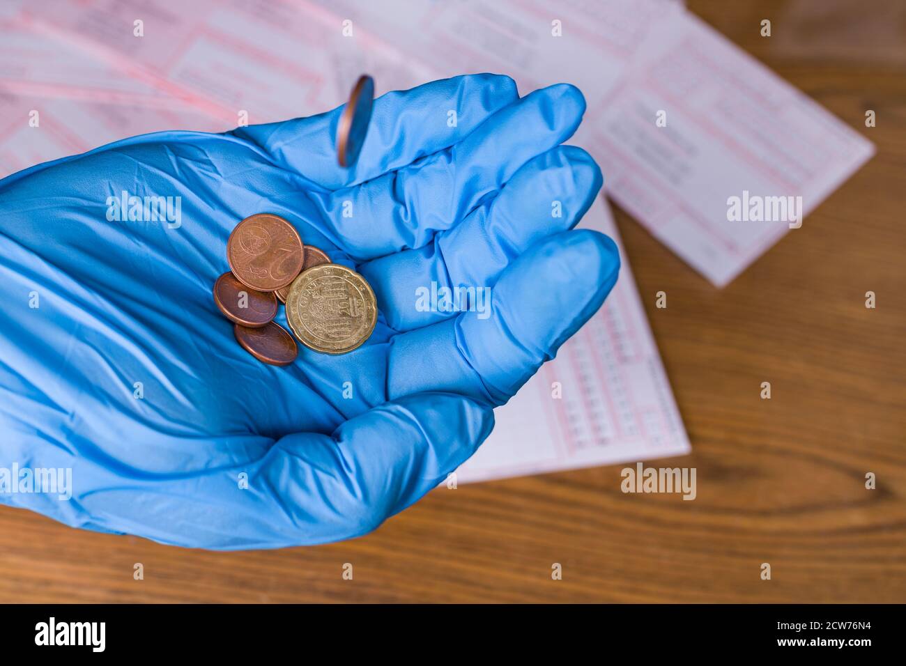 Kleine Metall-Euro-Münze in Handfläche fallen in blauen Schutzhandschuh. Geld in menschlicher Hand und Rechnungen im Hintergrund zählen. Arbeitsplatzverlust in der Coronavirus-Krise. Stockfoto