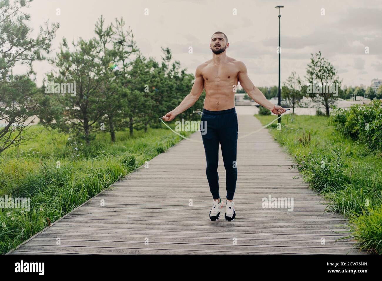 Sportlich muskulös Mann nutzt Springseil für Cardio-Training im Freien, hat perfekten Körper, atmet frische Luft und zeigt Ausdauer, arbeitet sich selbst de Stockfoto