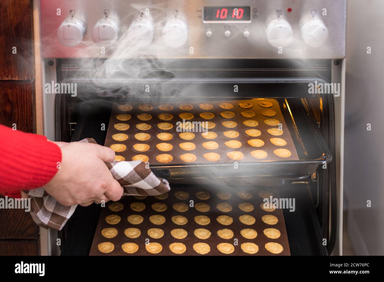 Hand nehmen heiße nussige Cookies aus dampfenden Konvektionsofen des Küchenofens. Frisch gebackener Buttergebäck in Silikonbackformen auf Blech. Stockfoto