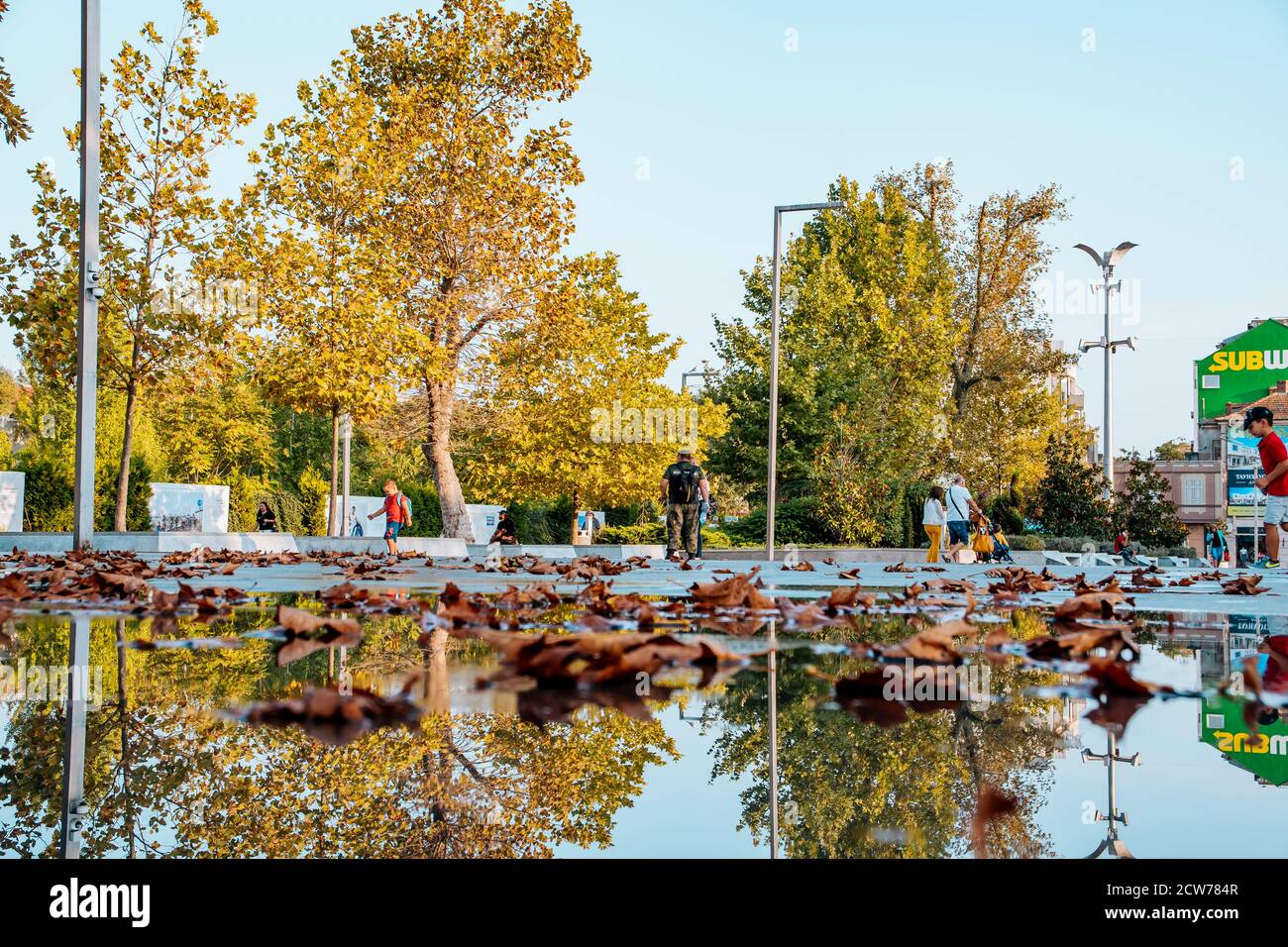 Burgas,Bulgarien 25.09.20:Regenwasser auf dem Boden spiegelt den Himmel und die Gebäude. Herbstblätter fallen ins Wasser. Stockfoto