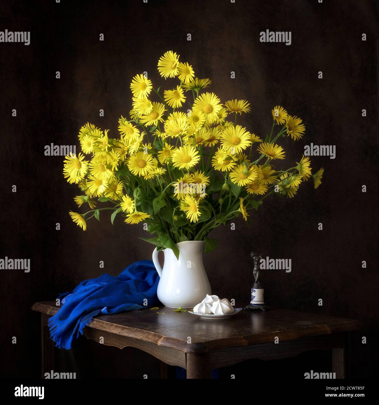 Frühling Stillleben gelb Gänseblümchen Studie mit blauem Schal und Weiße Kanne Stockfoto