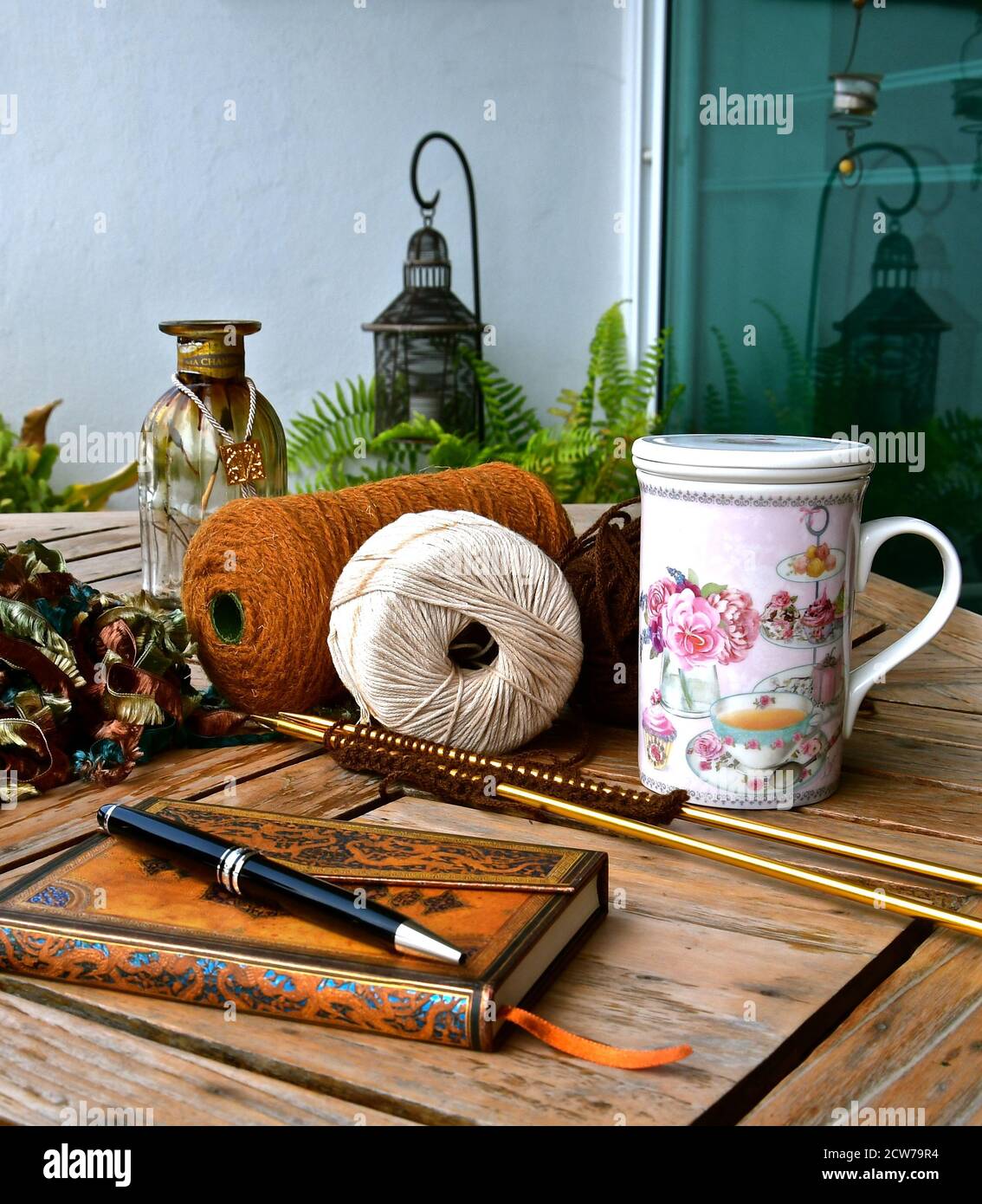 Konzept der Entspannung mit einem Leder gebunden Journal, verschiedene Strick-Accessoires, floral china Tee Tasse in einem Stillleben Komposition in einem rustikalen Garten Stockfoto