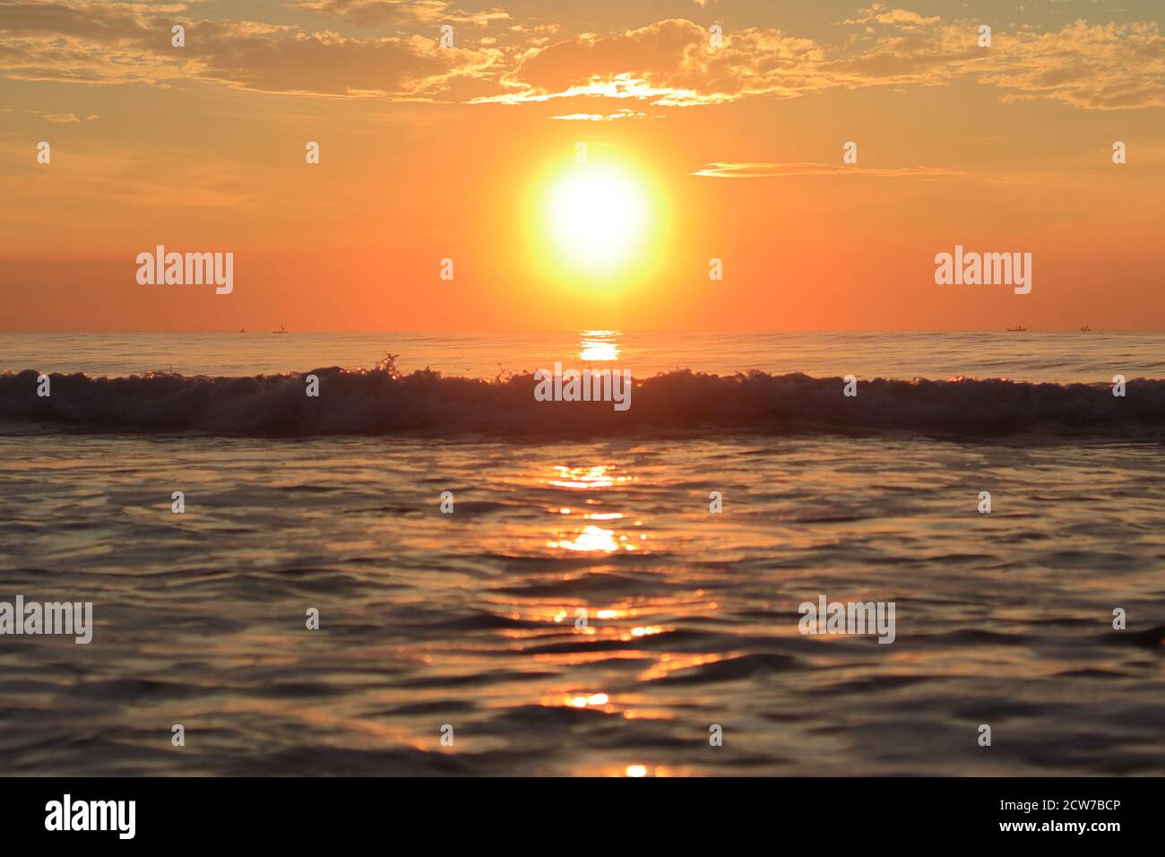 Bei Sonnenaufgang am Morgen, die riesigen hellen Strahlen der hellen Sonne begrüßen die aufgehenden Wellen des riesigen Ozeans Stockfoto