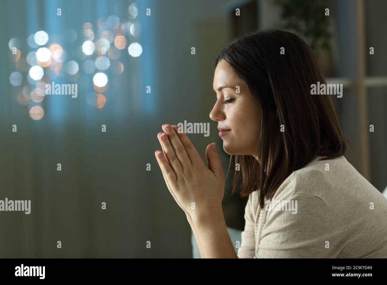 Profil einer christlichen Ordensfrau, die nachts im Sitzen betet Auf einer Couch im Wohnzimmer zu Hause Stockfoto