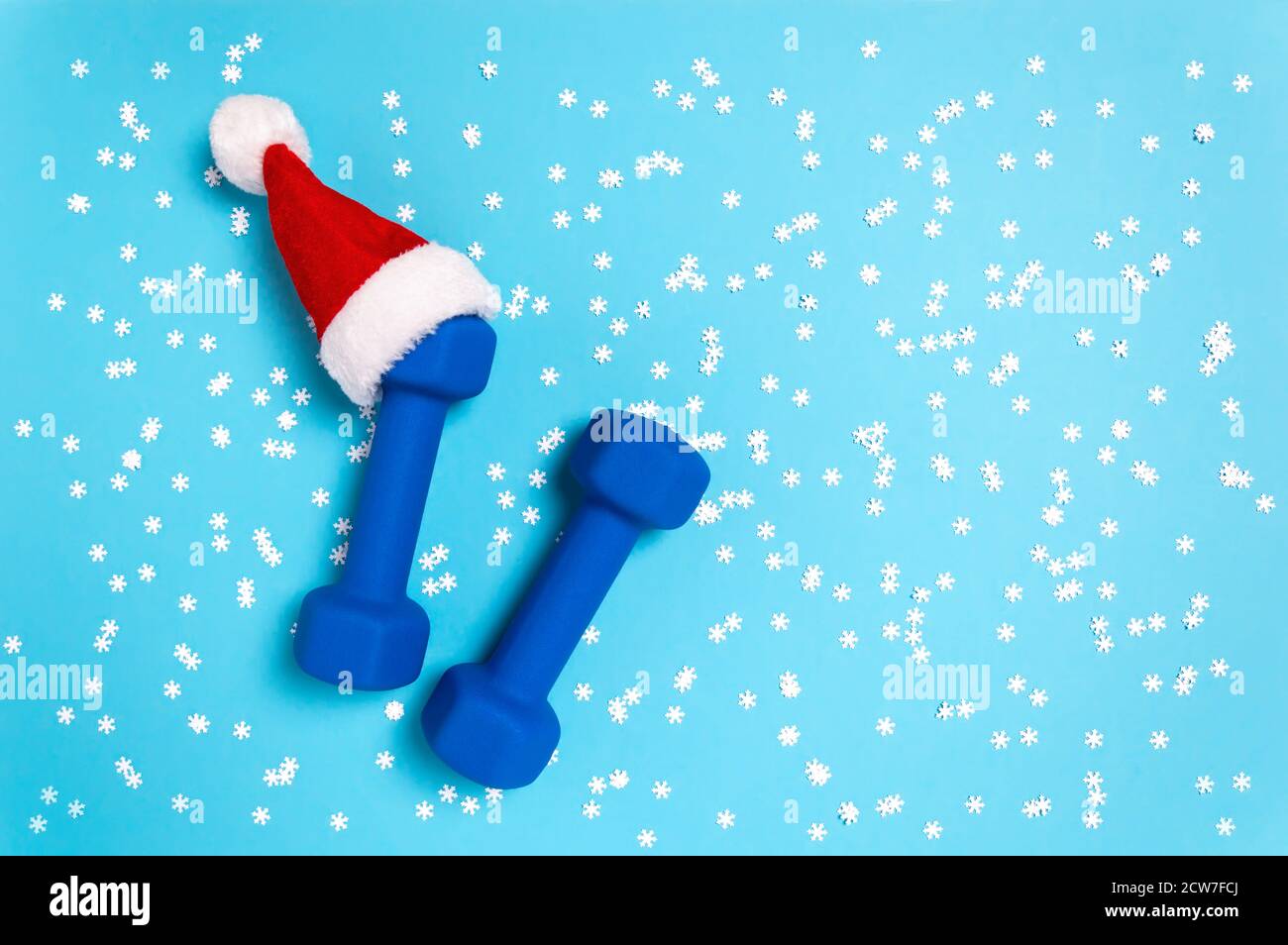Weihnachtssport flach lag mit Hanteln in rot Weihnachtsmann Hut auf blauem Hintergrund. Weihnachten und Neujahr Urlaubskonzept für Fitness, Training und gesund Stockfoto