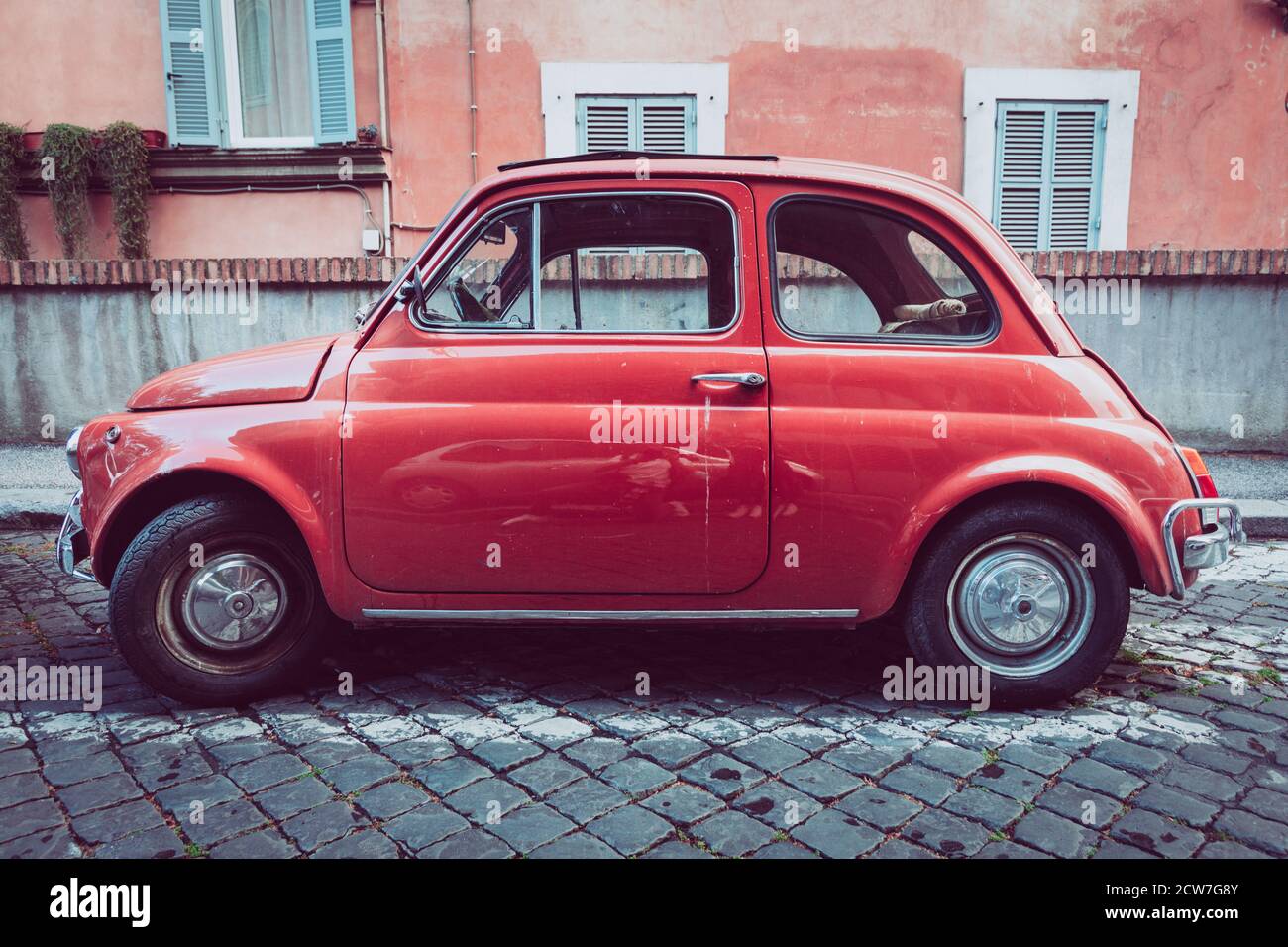 Alte kompakte italienische Auto Fiat 500 Cinquecento geparkt in der Altstadt von Rom in Italien. Orange Farbe, Pflaster mit Pflastersteinen. Stockfoto