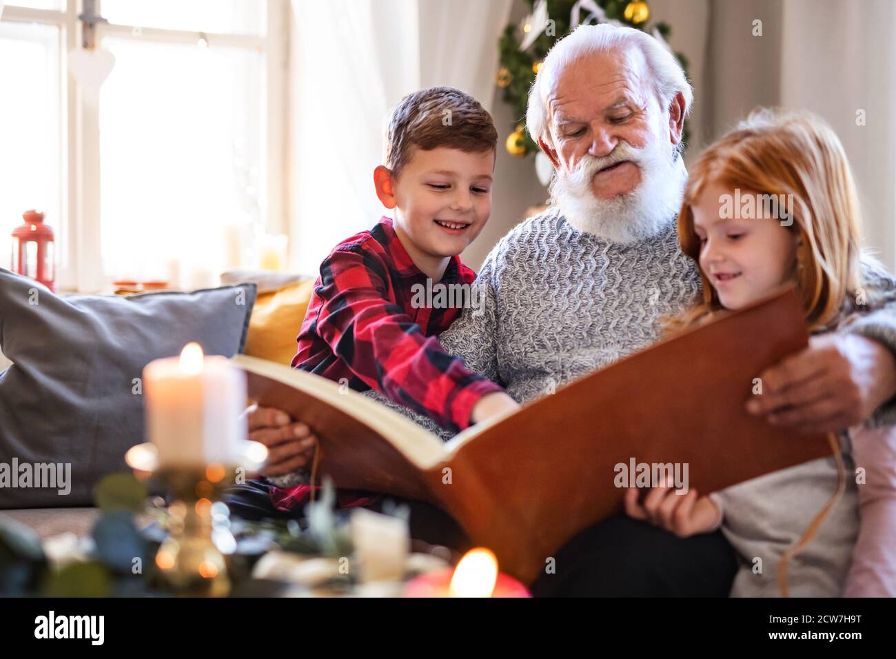 Kleine Kinder mit älteren Großvater drinnen zu Hause zu Weihnachten, Blick auf Fotos. Stockfoto