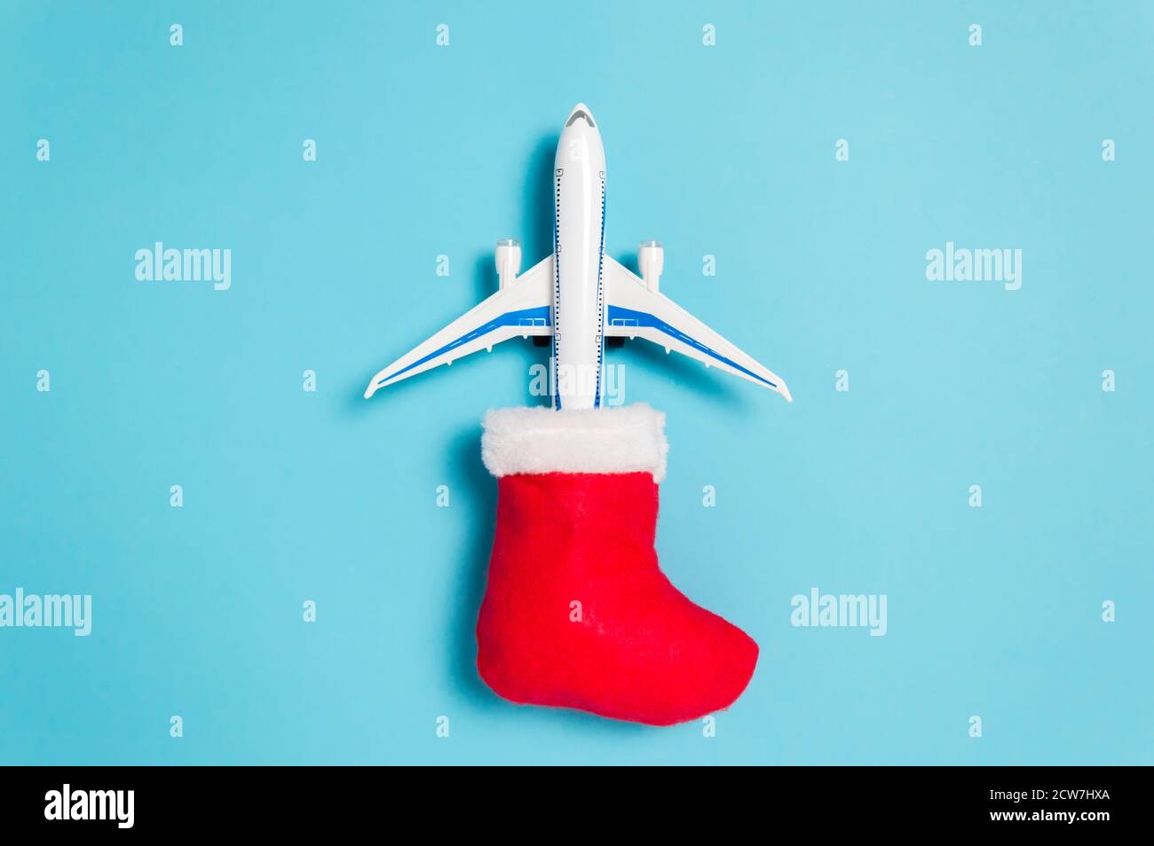 Weihnachtsferien Reisekonzept. Weißes Flugzeug, das aus roten Weihnachtsstrumpfsocken auf blauem Hintergrund fliegt. Flach Lay-Stil minimale Zusammensetzung für Trave Stockfoto