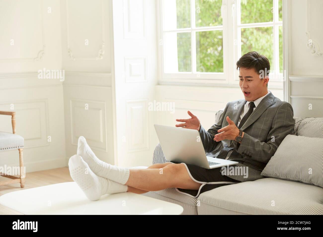 Junger asiatischer Geschäftsmann, der Anzug und Shorts trägt, von dem er arbeitet Heimbesprechung mit Kollegen online über Video-Chat auf Laptop Computer Stockfoto