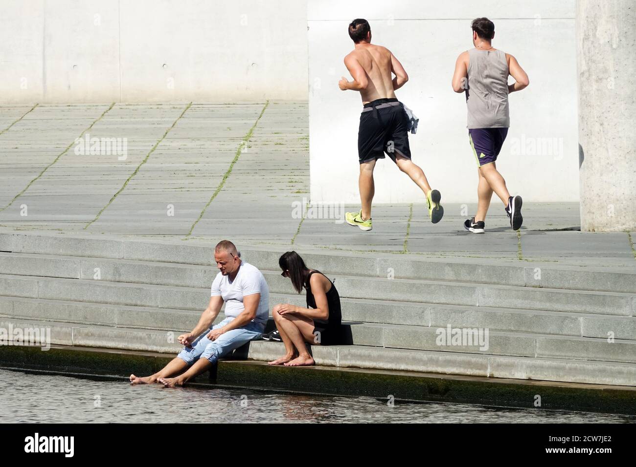 Berliner Stadtlebenspaar am Ufer der Spree Flussufer und im Hintergrund zwei Männer auf dem Laufen Stockfoto