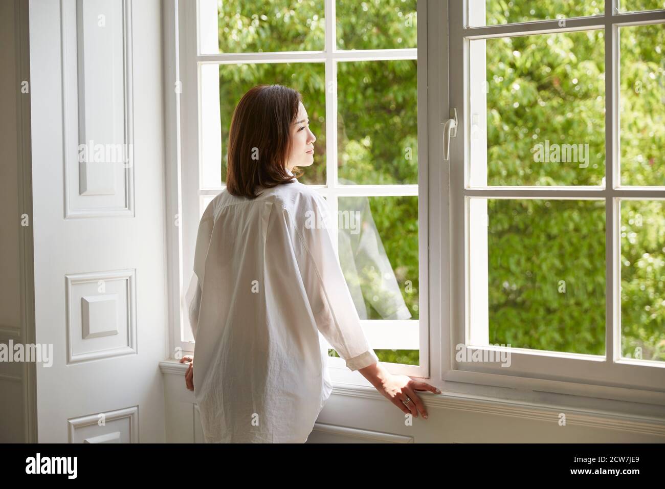 Rückansicht einer jungen asiatischen Frau, die herausschaut Fenster zu Hause Stockfoto