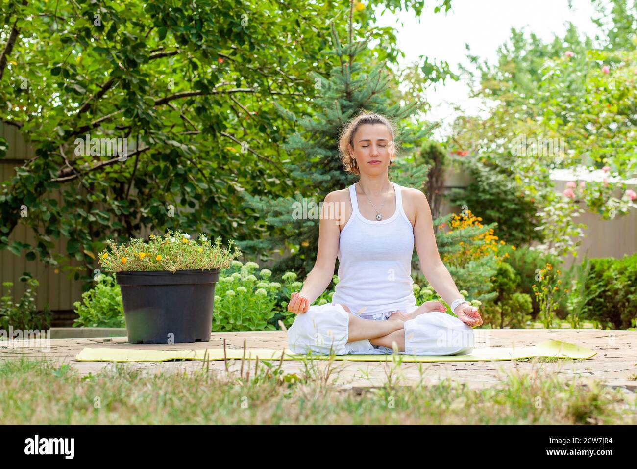 Die junge Frau praktiziert Yoga im Garten, sitzt in der LotusPosition