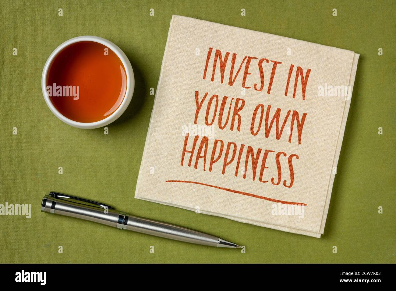 Investieren Sie in Ihr eigenes Glück - Handschrift auf Serviette mit einer Tasse Tee, Lifestyle und persönlichem Entwicklungskonzept Stockfoto