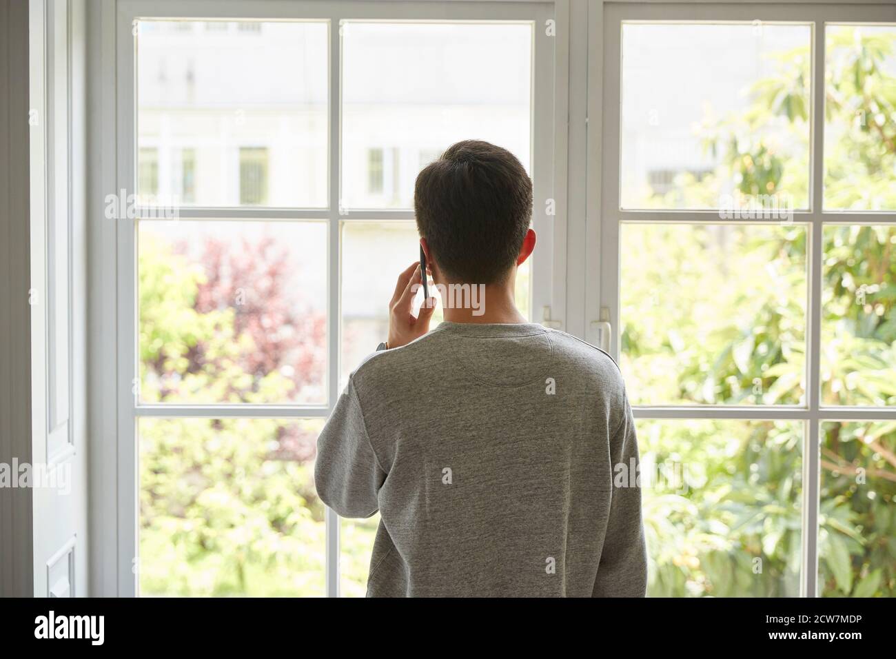 Rückansicht eines jungen asiatischen Mannes, der aus dem Fenster schaute Beim Telefonieren mit dem Handy Stockfoto