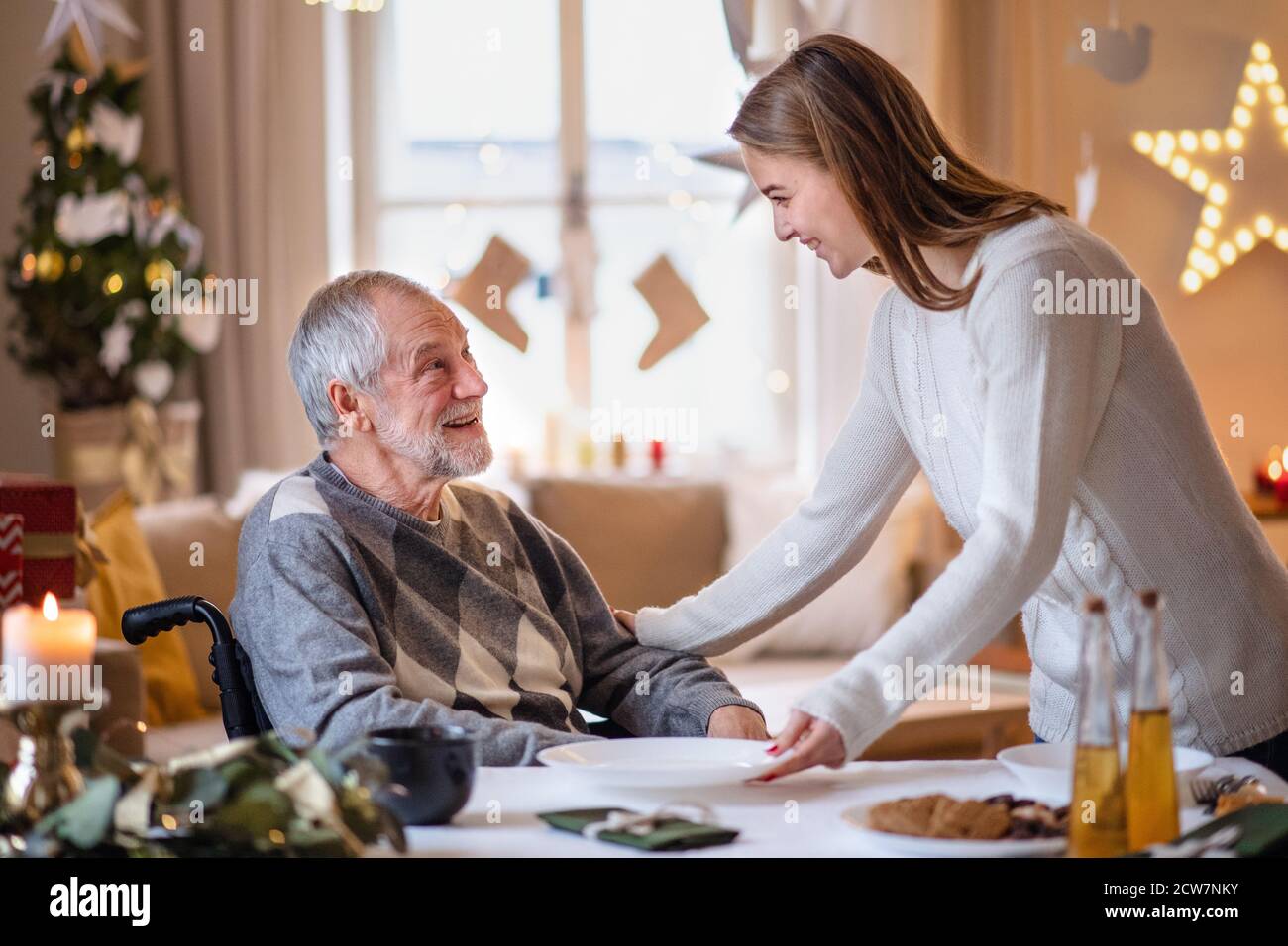 Junge Frau mit älteren Großvater im Rollstuhl drinnen zu Hause zu Weihnachten. Stockfoto