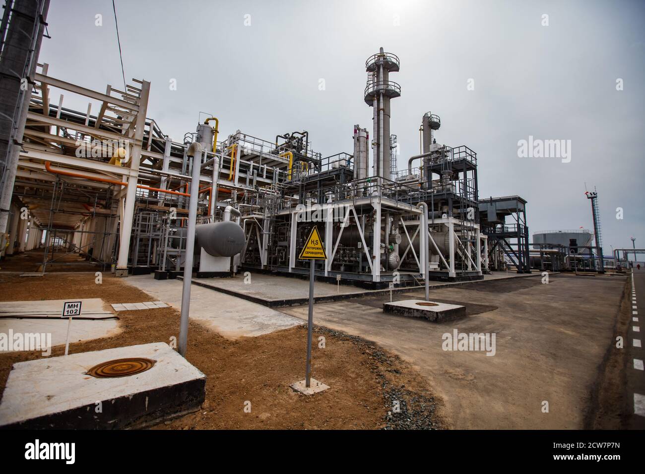 Ölraffinerie und Gasverarbeitungsanlage in der Wüste auf dem gelben Sand. Distilin Türme und Pipelines. Gelbes Warnschild für Schwefeldioxid (Schwefel). Stockfoto