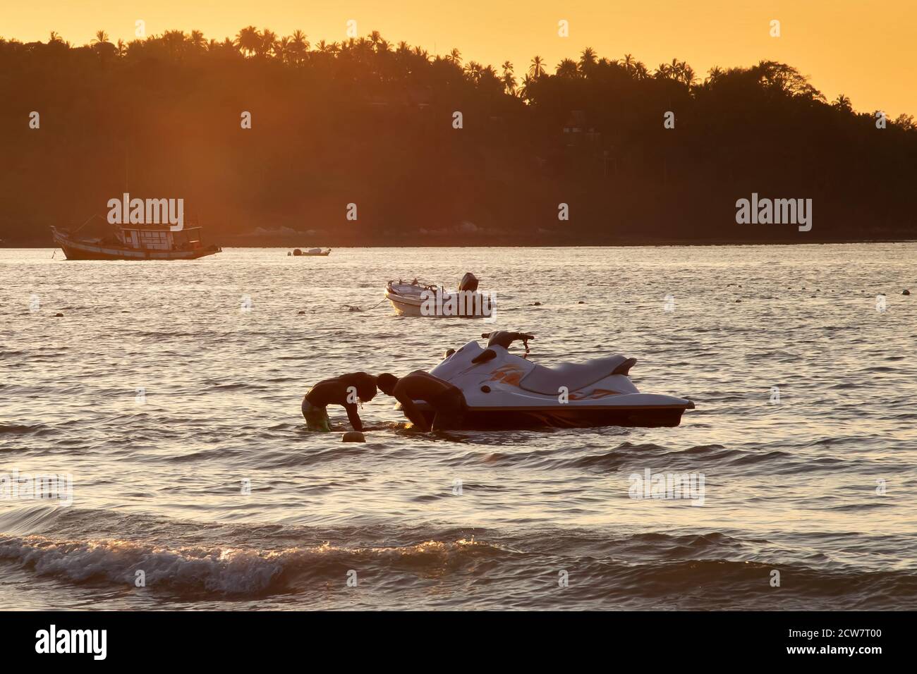 Zwei Herren bei Sonnenuntergang ziehen Hydrocycle aus dem Wasser. Sommerurlaub. Wasserfahrrad auf einen Anhänger geladen Stockfoto