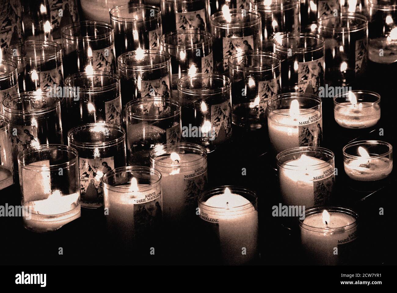 Fackeln des Glaubens: Flackernde Votivkerzen erleuchten kleine Räume im dunklen Innenraum der Basilika Ste-Marie-Madeleine (Basilika Santa Maria Magdalena) in Vézelay, Yonne, Burgund, Bourgogne-Franche-Comté, Frankreich. Die Basilika ist die Kirche einer ehemaligen Benediktinerabtei, die im 12. Jahrhundert umgebaut und erweitert wurde, um mit Horden von Pilgern fertig zu werden, die zur Verehrung der in der Krypta erhaltenen Knochen reisen, die als Reliquien der Heiligen Maria Magdalena gedacht sind. Stockfoto