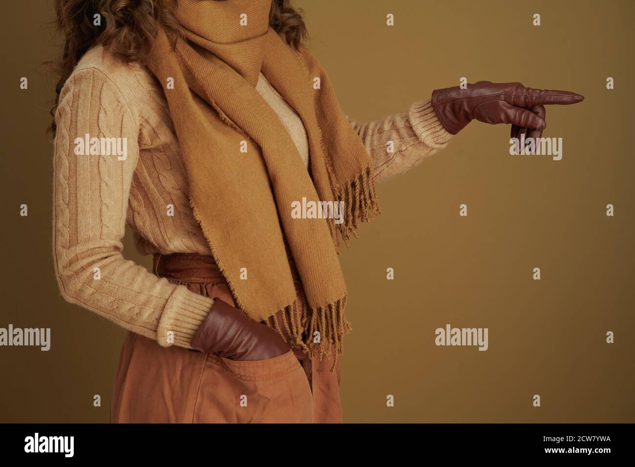 Hallo Herbst. Nahaufnahme einer Frau im Schal mit Lederhandschuhen, die auf etwas vor beigem Hintergrund zeigen. Stockfoto