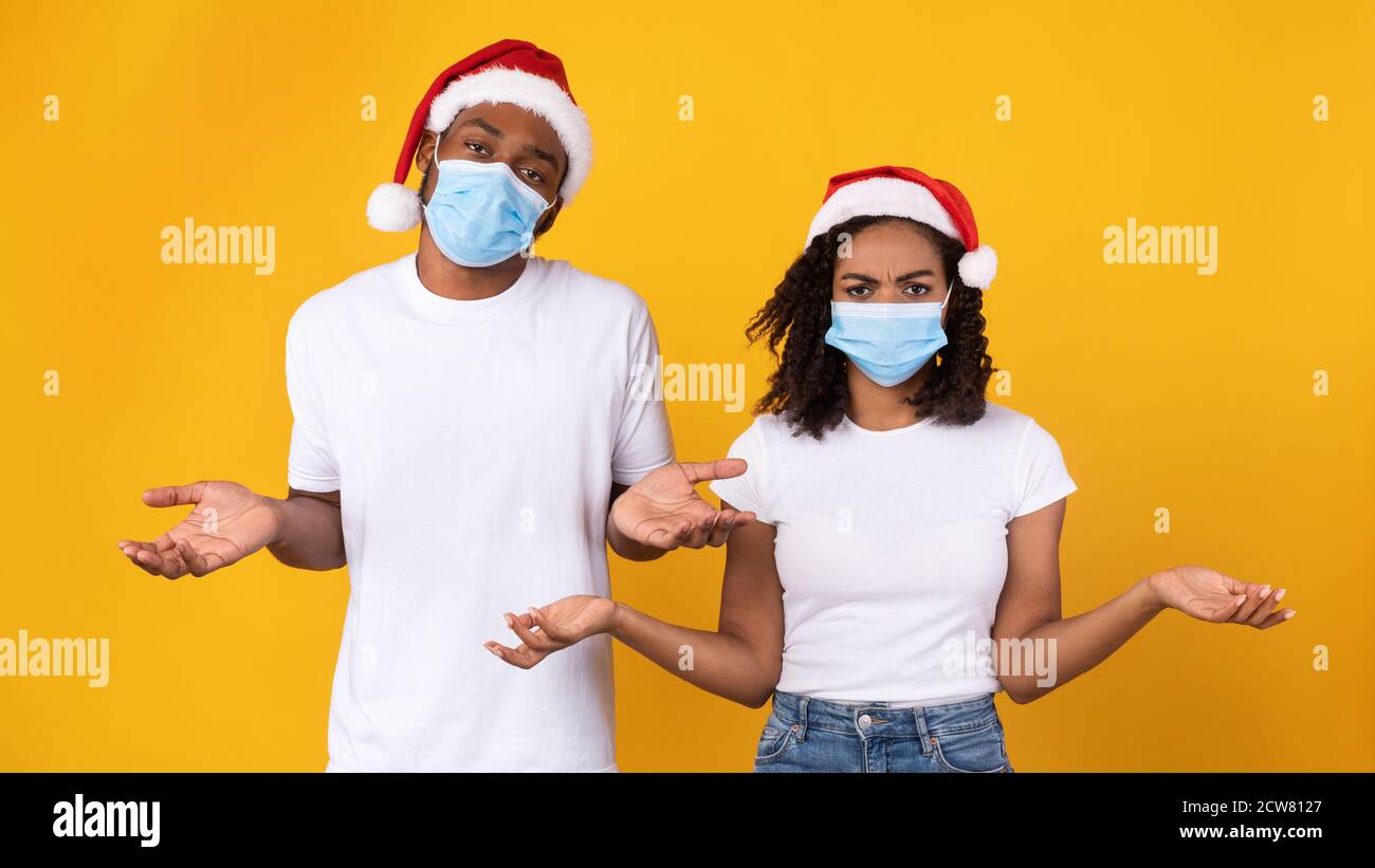Schwarzes Paar Trägt Coronavirus Masken Und Weihnachtshützen, Gelber Hintergrund Stockfoto