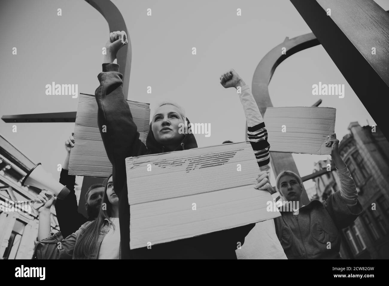Schwarz und Weiß. Gruppe von Aktivisten, die Slogans in einer Kundgebung geben. Kaukasische Männer und Frauen marschieren zusammen in einem Protest in der Stadt. Schauen Sie wütend, hoffnungsvoll, zuversichtlich. Leere Banner für Ihr Design oder Ihre Anzeige. Stockfoto