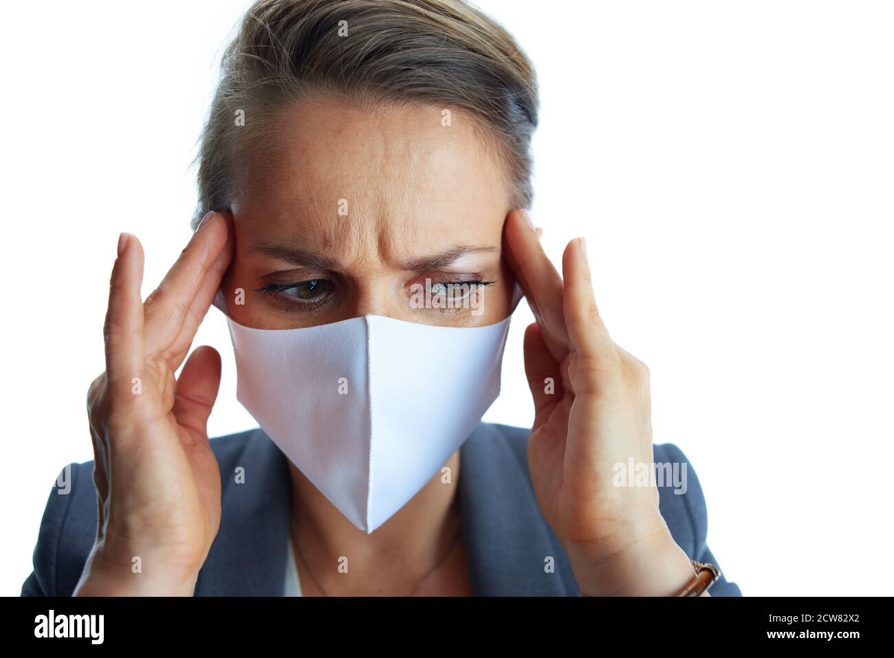 Geschäft während covid-19 Pandemie. Betonte junge Geschäftsfrau in einem grauen Anzug mit medizinischer Maske isoliert auf weiß. Stockfoto