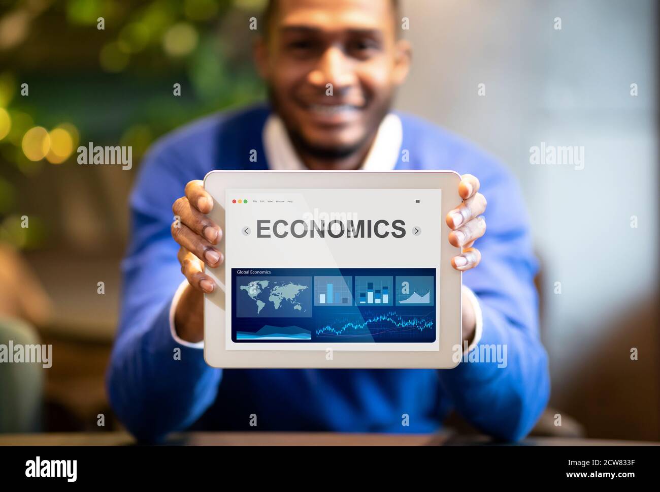 Black Geschäftsmann Zeigt Digital Tablet Mit Wirtschaft Grafiken Sitzen Im Innen Stockfoto