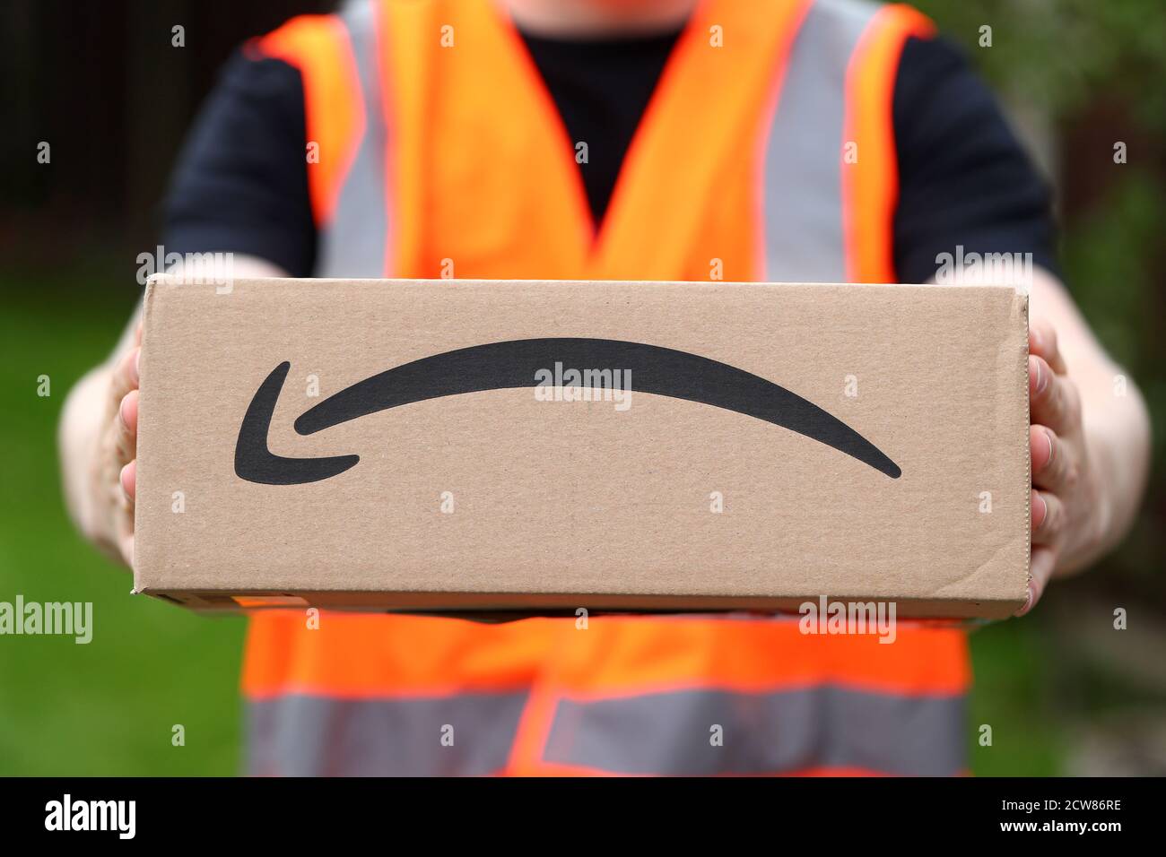 Ein Mann liefert eine Amazon-Box mit dem Amazon Lächeln Logo in Großbritannien Stockfoto
