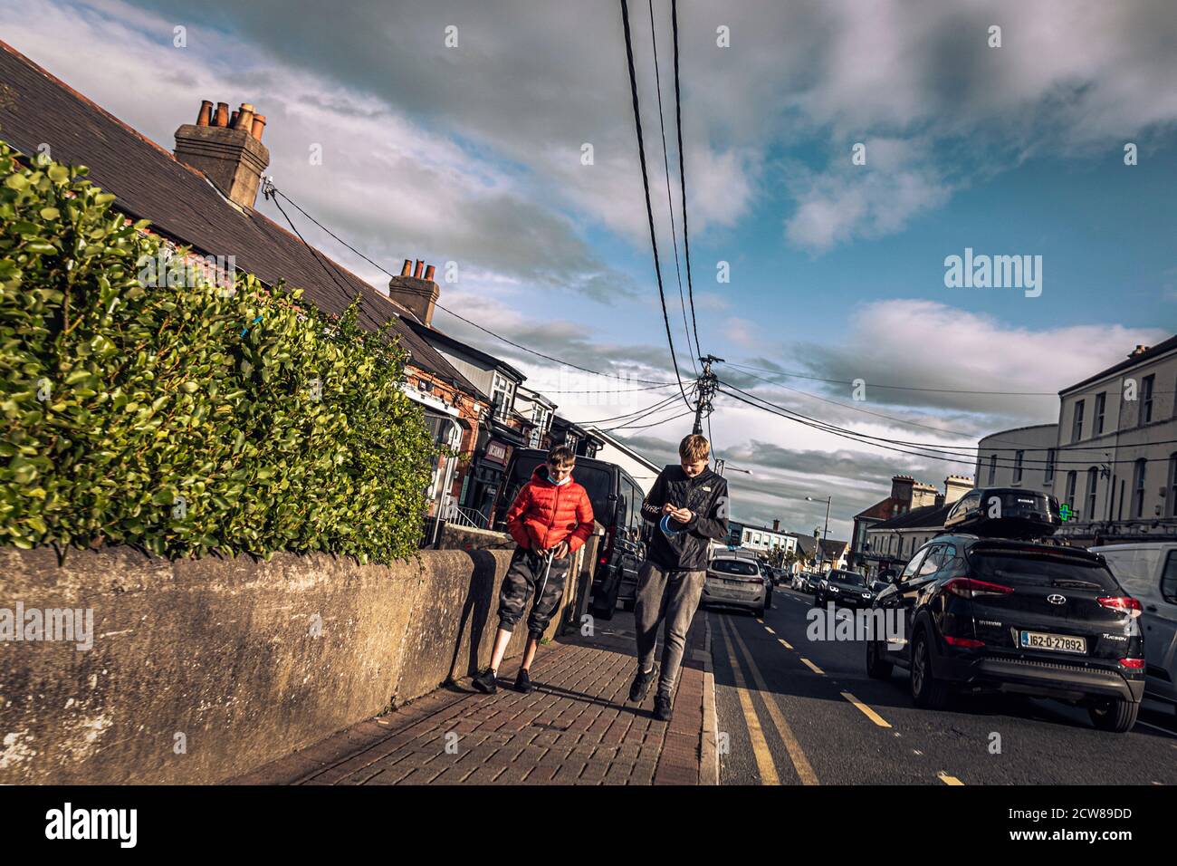 Alltag. Teenager, die auf der Main Street spazieren und mit klarem Gesichtsschild herumbasteln. Greystones. Irland Stockfoto
